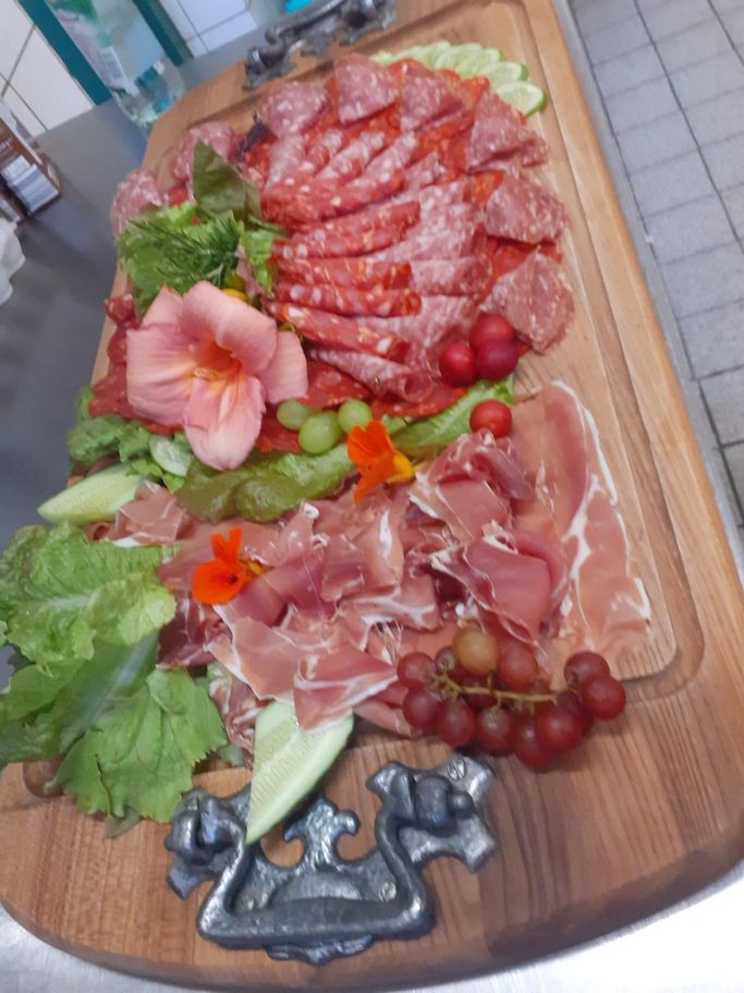 Rustikale Brotzeit Platte aus Holz mit Salami, Schinkensorten, Gurken und Salat Deko.